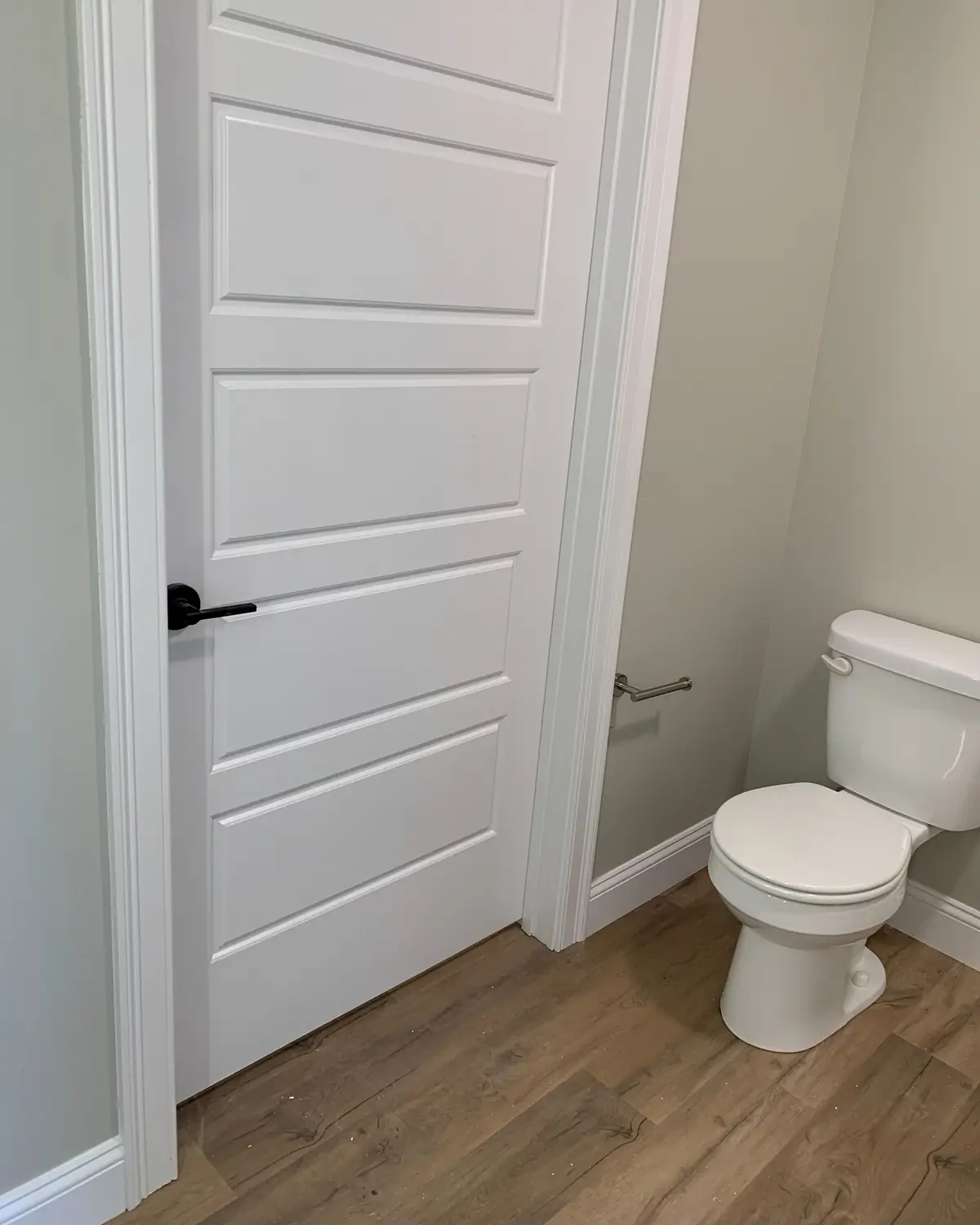 Bathroom doorway with a new white panel door, casing and baseboard over wood look flooring