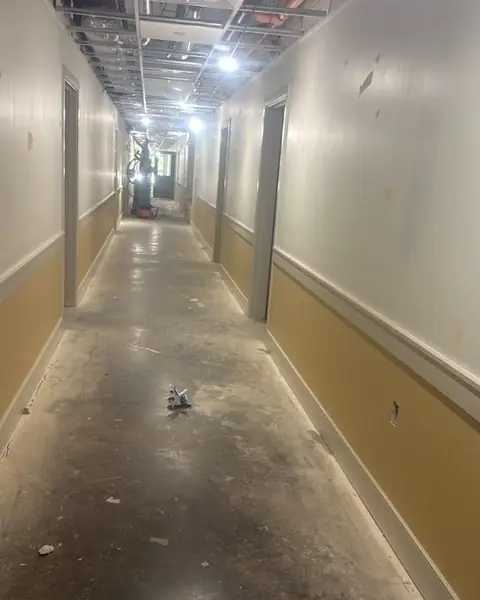 Long hallway during interior demolition, ceiling opened to the framing and floor stripped to concrete