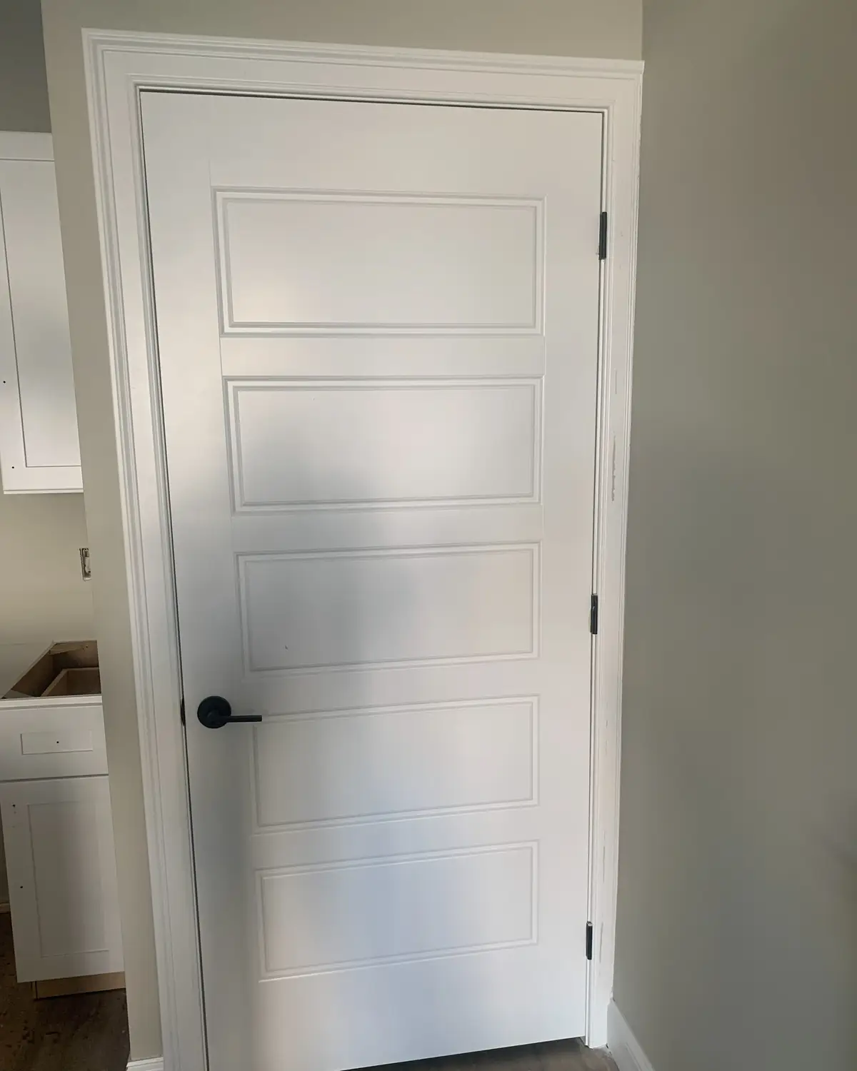 White five panel interior door with new casing and a black lever handle, installed by Santos General Contractors