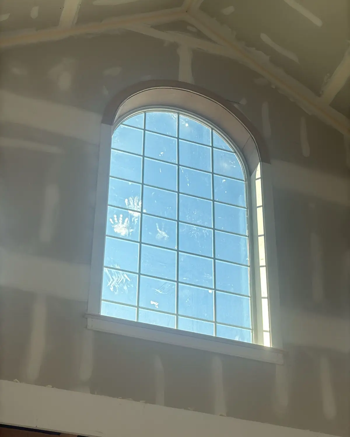 New drywall taped and finished around an arched window, ready for trim and paint