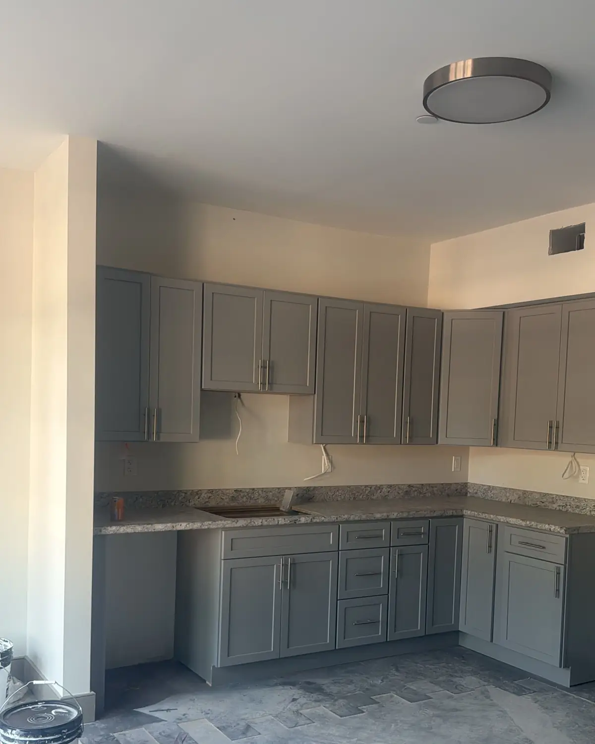 Gray shaker kitchen cabinets installed in an L shape, before the new floor goes in